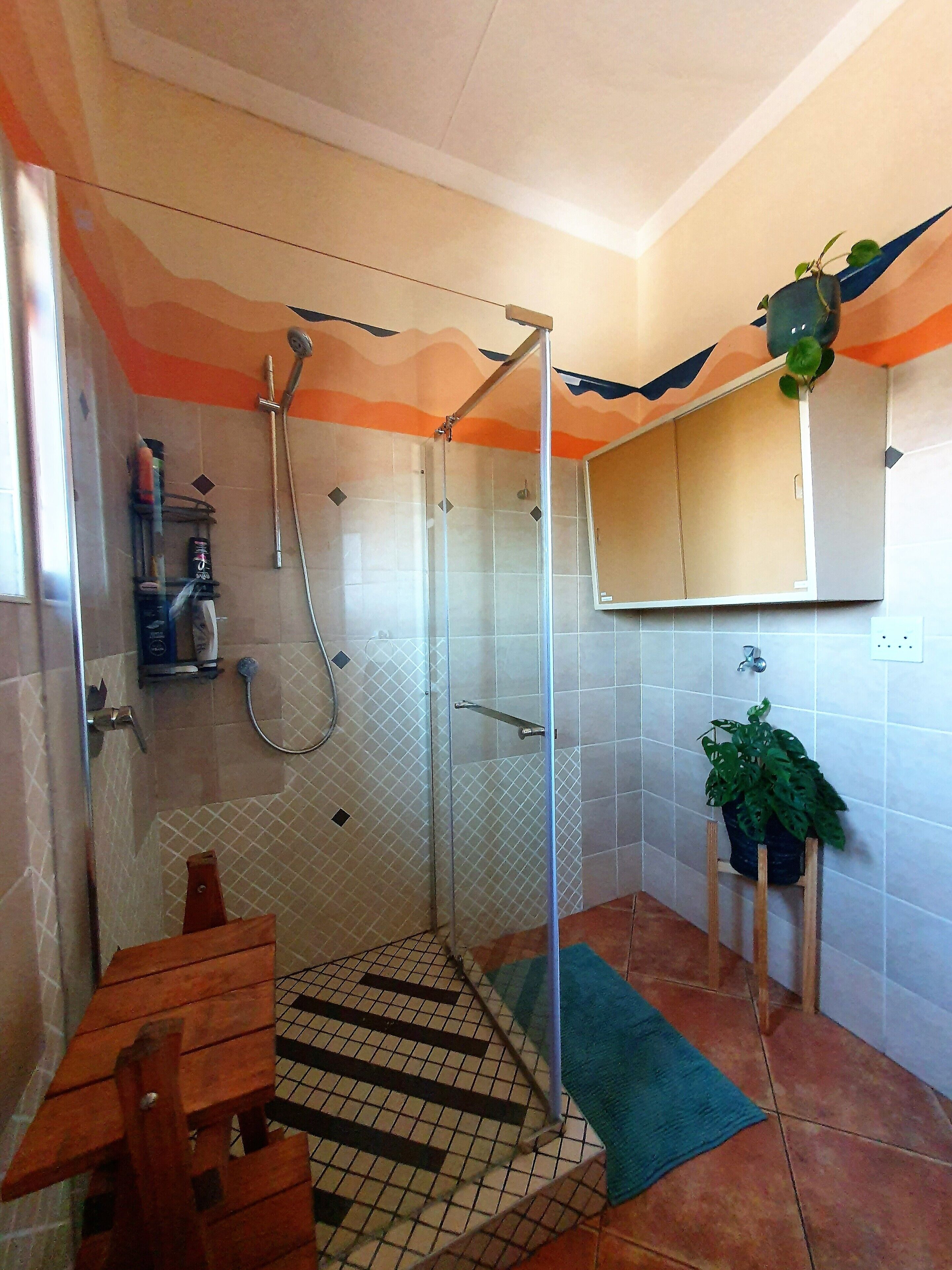 A bathroom with a shower, a wooden bench, a green plant, and a tiled floor.