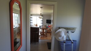 A hallway leading to a dining area with a table and chairs, a large mirror, and a hat hanging on a hook. - Seaside Nest on Private Waterfront (Chéticamp)