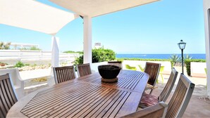 A wooden table with chairs and a black pot in the center, set on a patio with a view of the sea. - Villa XOROI- Dream front line Villa in Betlem (Mallorca) with pool and direct access to the sea. - Free Wifi (Artá)