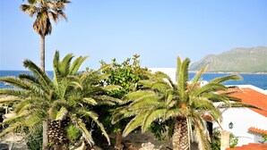 A coastal view with palm trees and a building with a red-tiled roof. - Villa XOROI- Dream front line Villa in Betlem (Mallorca) with pool and direct access to the sea. - Free Wifi (Artá)