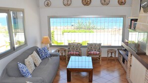 A living room with a sofa, two armchairs, a coffee table, and a view of the beach through a large window. - Villa XOROI- Dream front line Villa in Betlem (Mallorca) with pool and direct access to the sea. - Free Wifi (Artá)