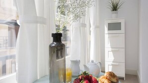 Ein helles Zimmer mit einem für ein Frühstück gedeckten Tisch, inklusive Flasche, Krug, Teekanne und Gebäck.
