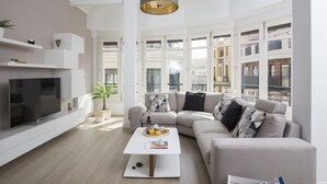 Ein modernes Wohnzimmer mit Flachbildfernseher, Couchtisch, Sofa und Pendelleuchte.