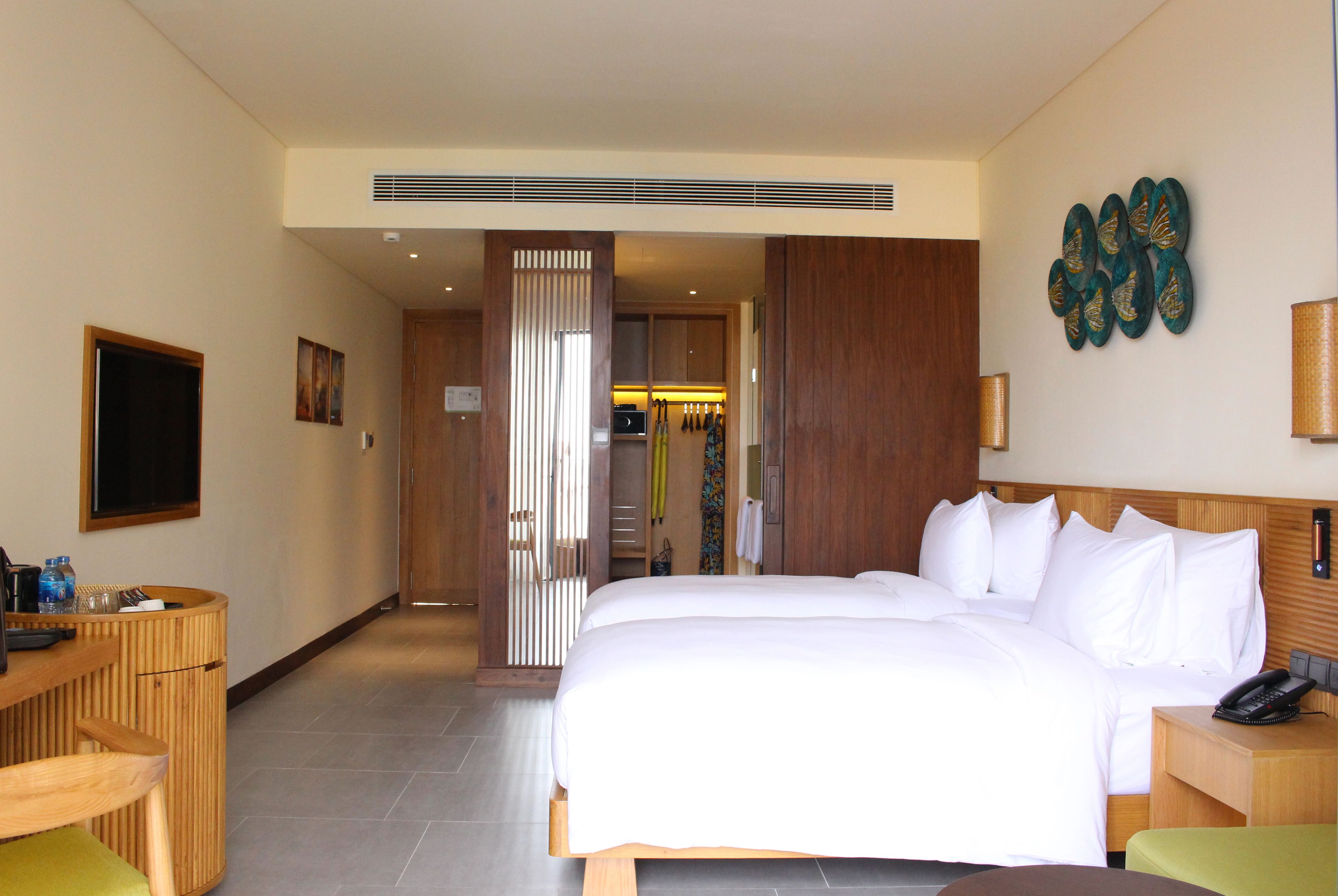 Habitación de hotel con una cama grande, un escritorio con silla, un televisor y un elemento decorativo en la pared.