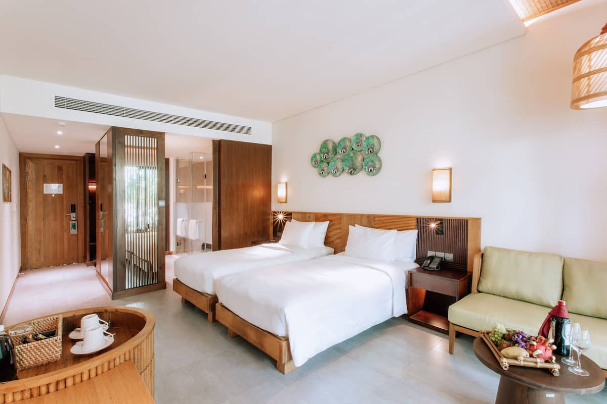 A hotel room with two beds, a sofa, a dining table, and a decorative wall piece.