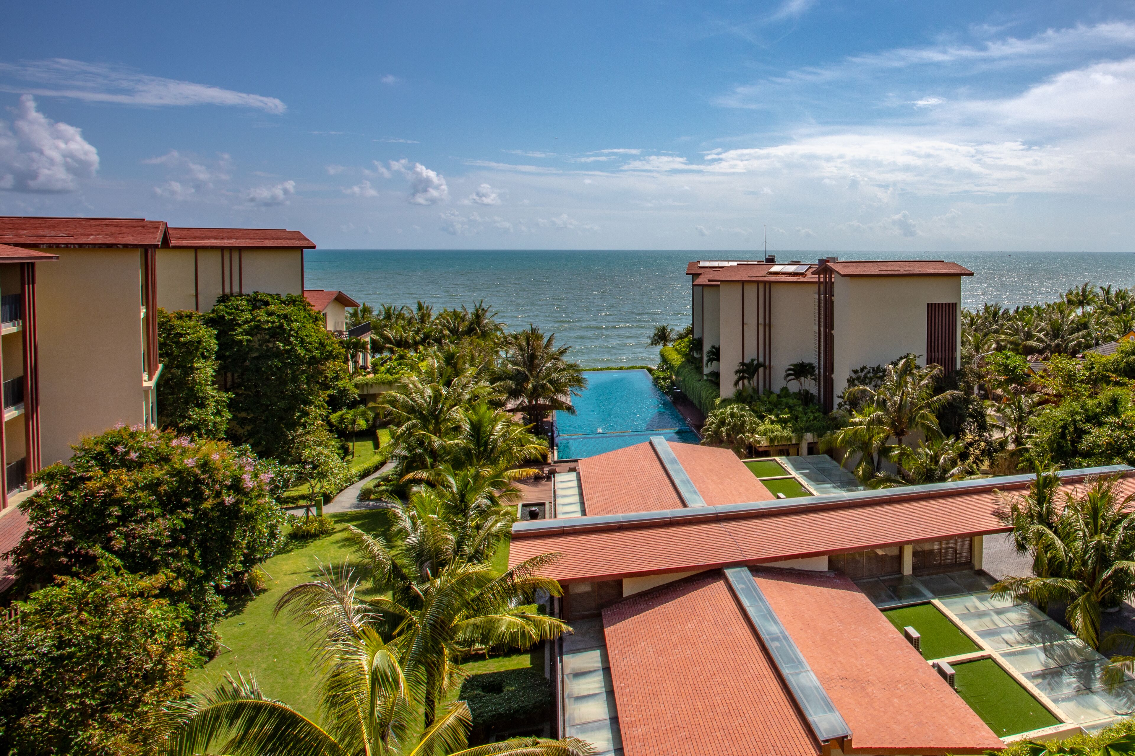 A resort with a pool, palm trees, and a view of the ocean.