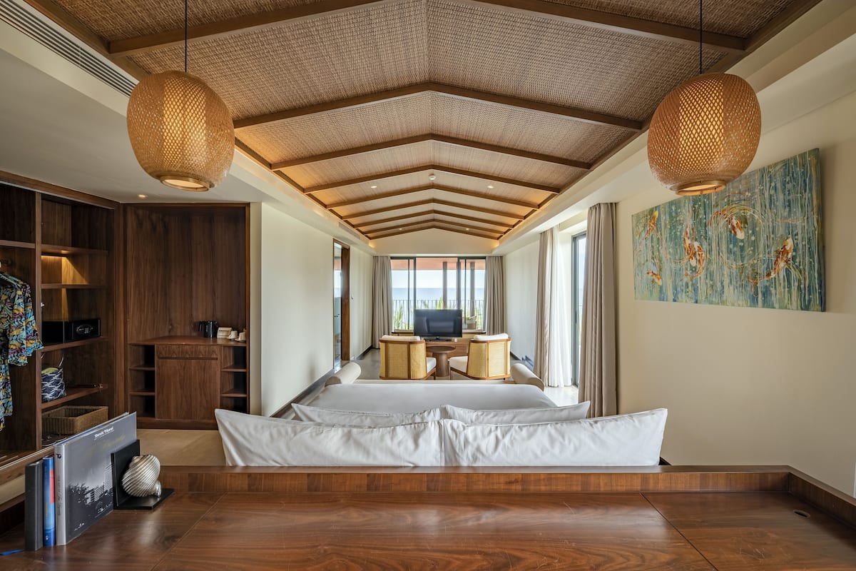 A spacious room with a large bed, wooden ceiling, and a television in the background.