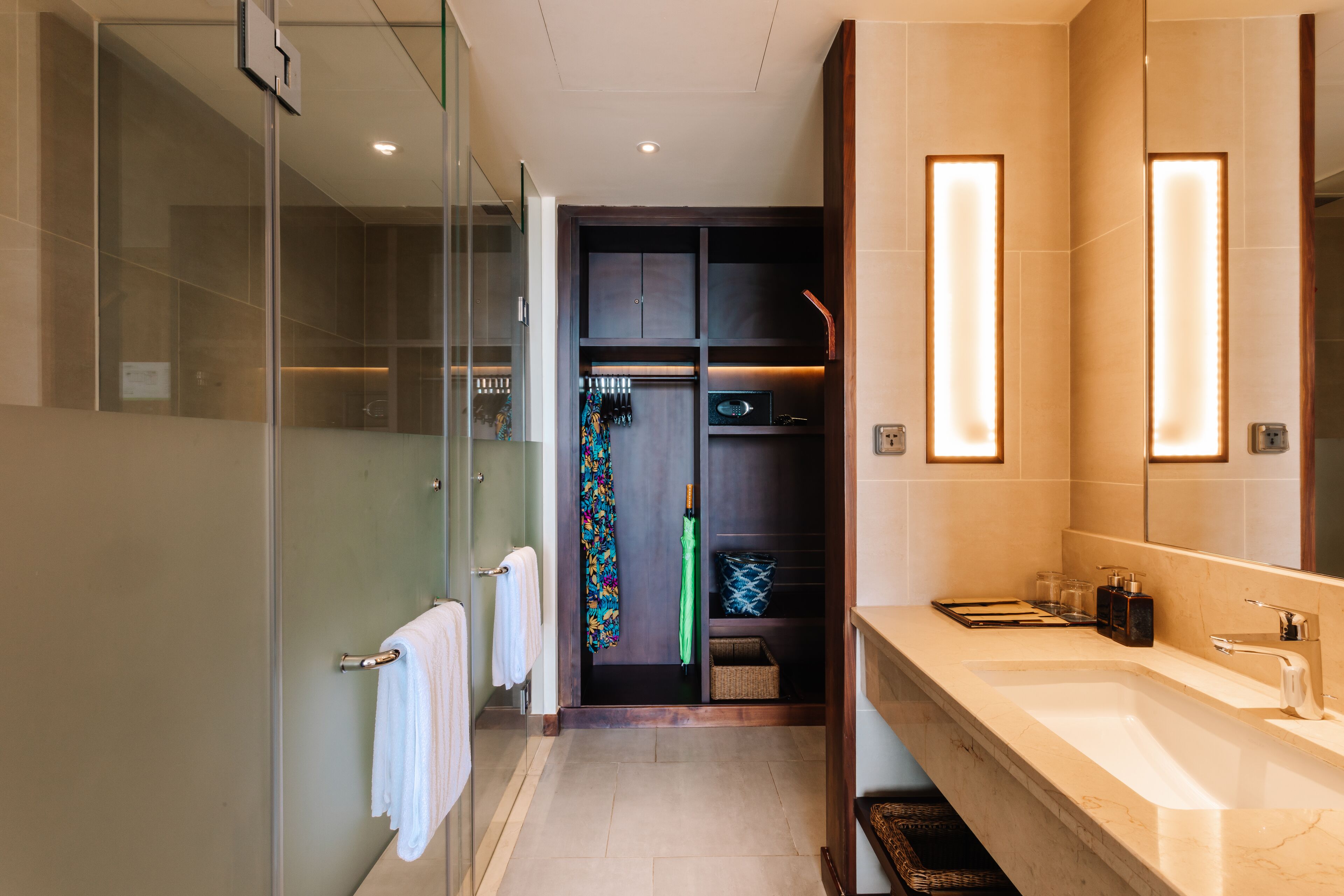 Une salle de bain moderne dotée d’une douche à parois de verre, d’un meuble-lavabo avec un grand miroir et d’un dressing avec un portant à vêtements.