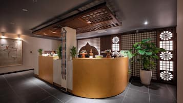 Ein Empfangsbereich mit einem gebogenen Holztisch, Blumentöpfen und einem traditionellen japanischen Bildschirm.
