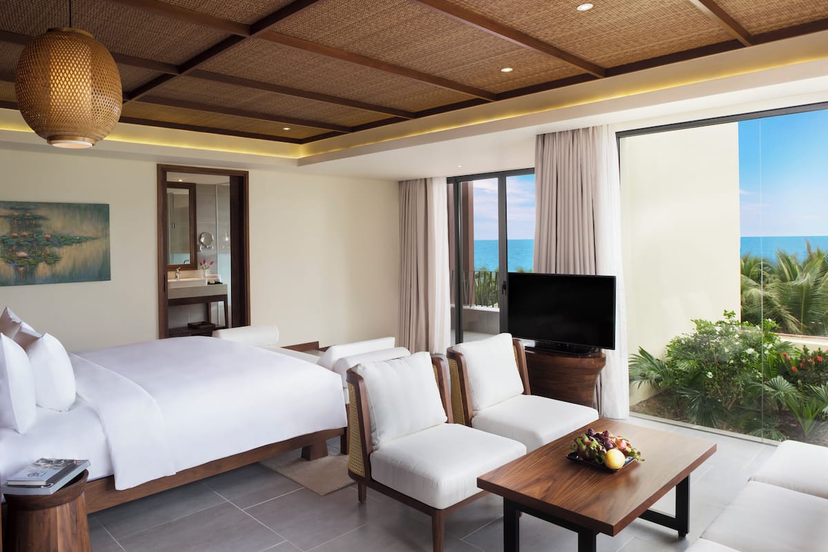 A hotel room with a bed, two sofas, a TV, and a balcony with a view of the sea.