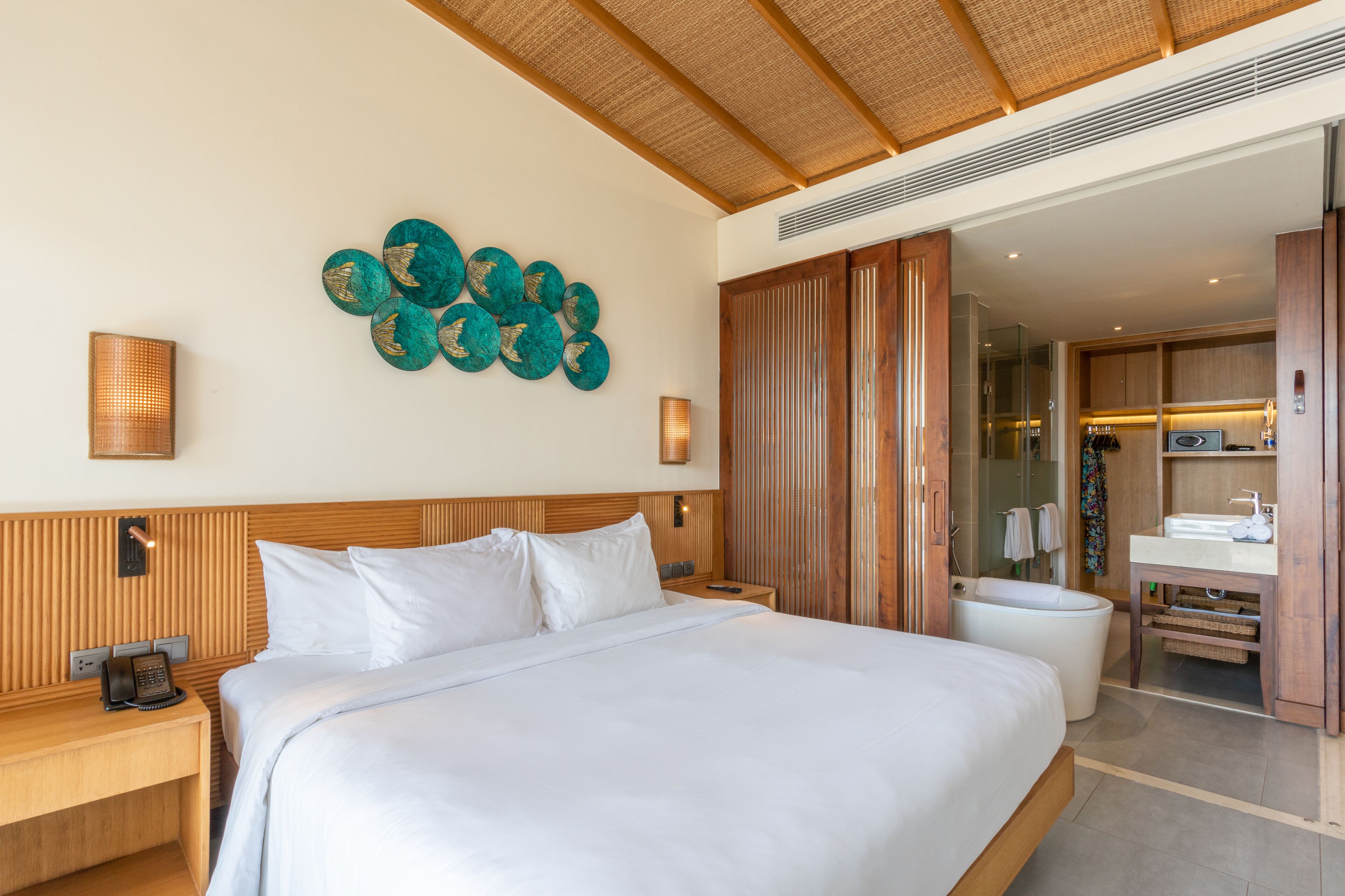 Une chambre d’hôtel avec un grand lit, une tête de lit en bois, un téléphone fixé au mur et une salle de bain équipée d’une baignoire et d’un lavabo.