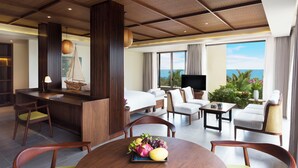 A modern hotel room with a large bed, a dining area with a fruit bowl, a living area with a sofa and armchairs, a TV, and a balcony with a view of the ocean. - Dusit Princess Moonrise Beach Resort (Phu Quoc)