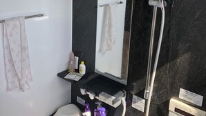 Un bany modern amb una paret de marbre negre, un lavabo blanc, un mirall, una dutxa i diferents productes de tocador.