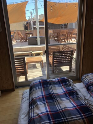 A room with a large sliding glass door leading to an outdoor deck with wooden furniture and a canopy. - RSD village - Hostel (Miura)