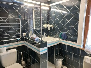 A bathroom with a black and white tiled wall, a white sink, a mirror, a towel rack, a toilet, and a trash bin.