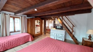 Un dormitorio con dos camas, techo de madera, kitchenette y una escalera.