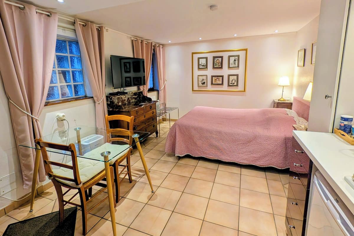 A bedroom with a bed, a desk, a chair, a TV, and a window.
