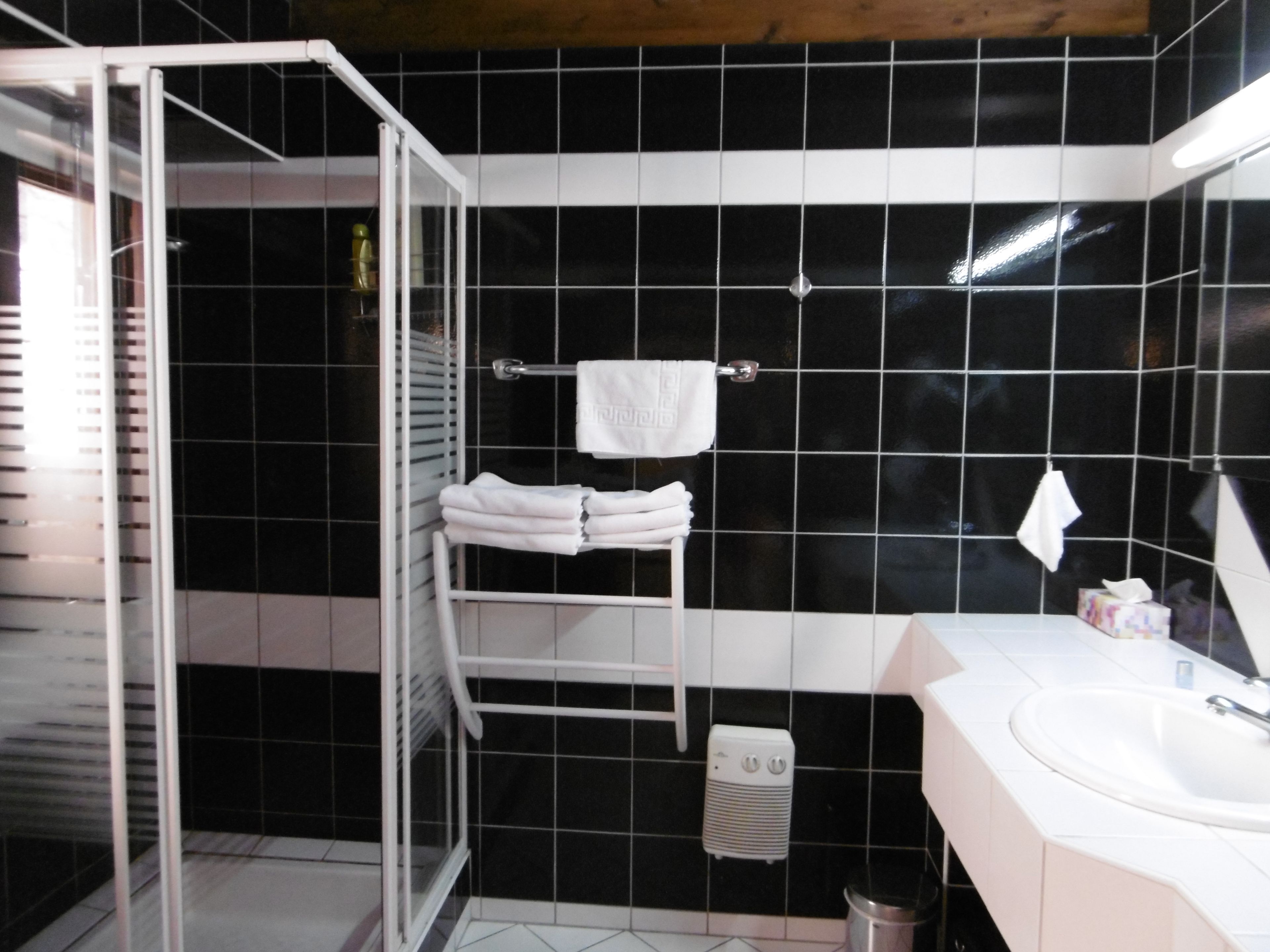 Un baño con azulejos negros, un lavamanos blanco y un perchero para toallas.
