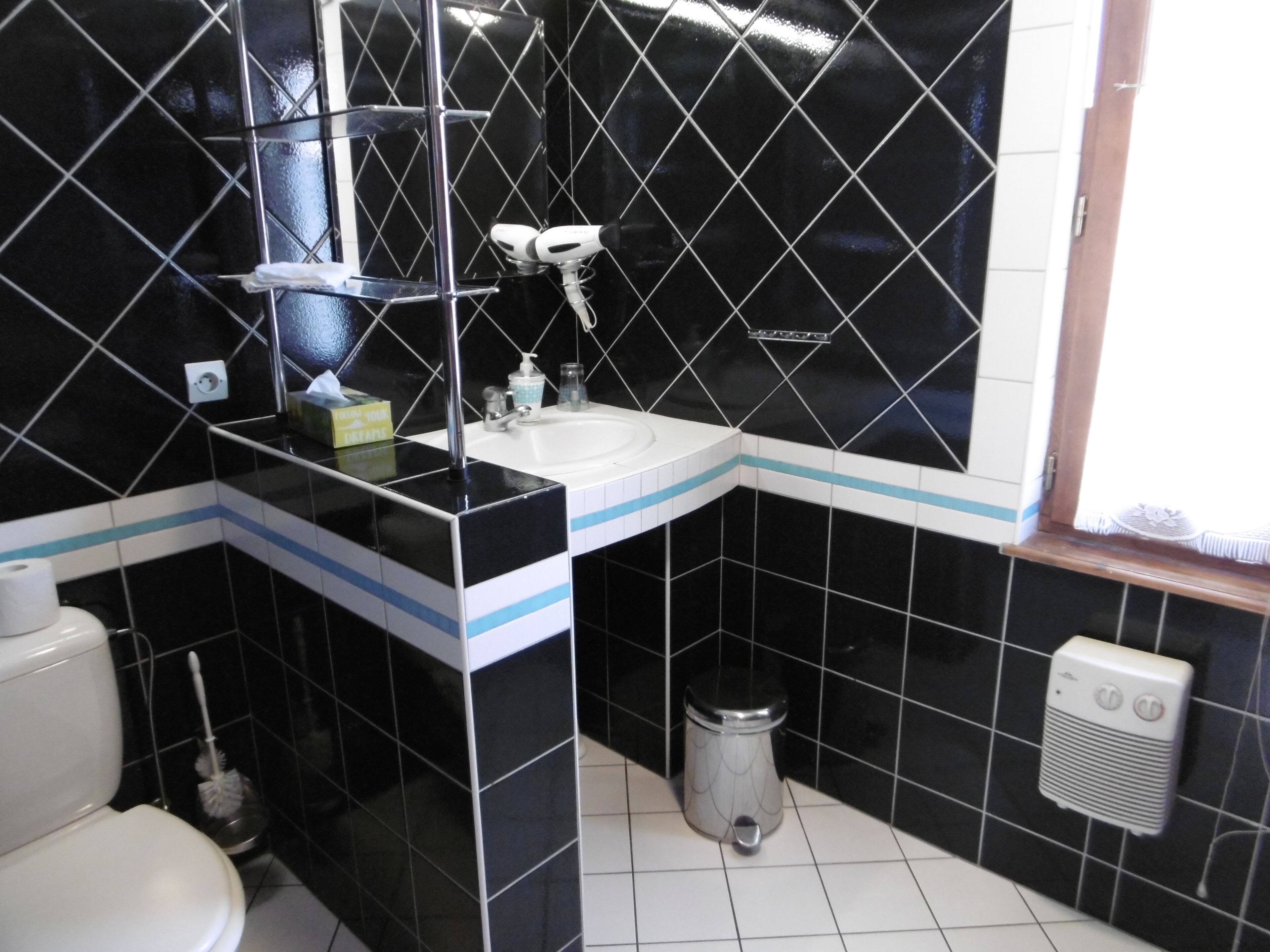 Een badkamer met een zwart-wit betegelde vloer, een wit wastafelmeubel, een spiegel en een prullenbak.