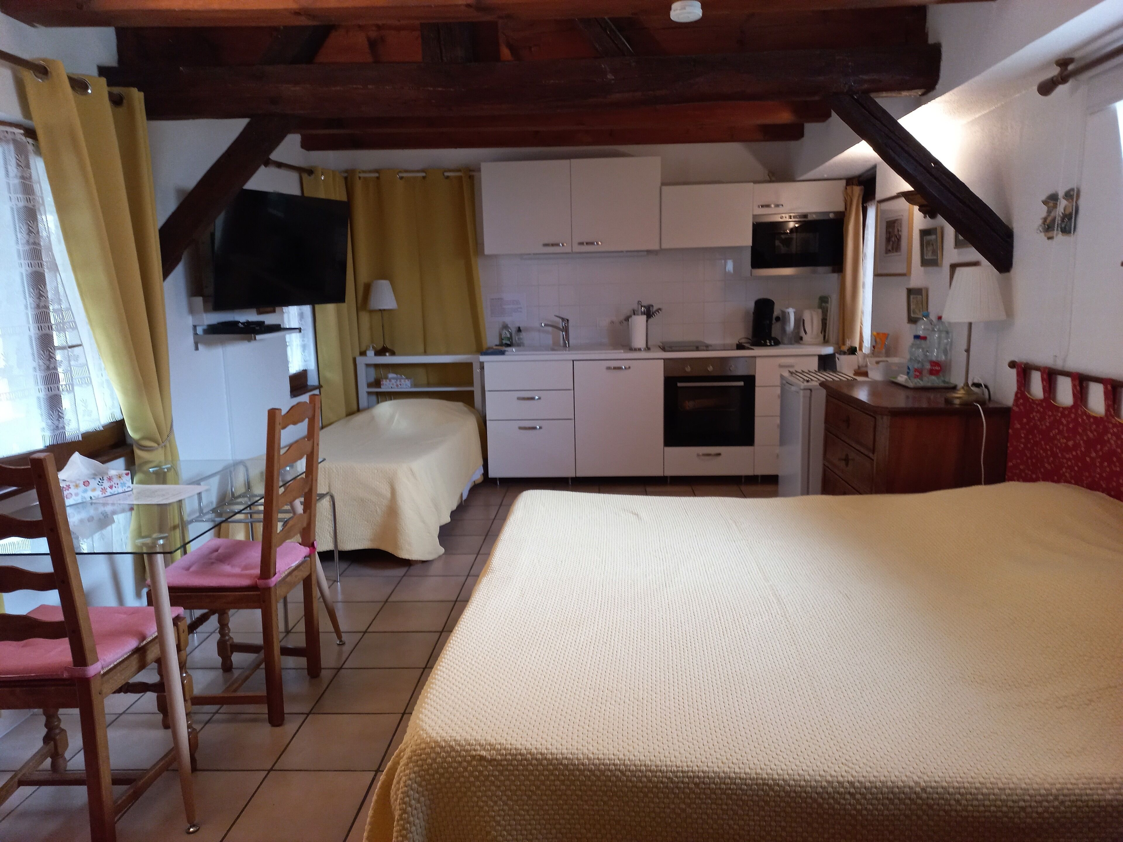 Un dormitorio con cama, una kitchenette pequeña, un comedor con sillas y un televisor montado en la pared.