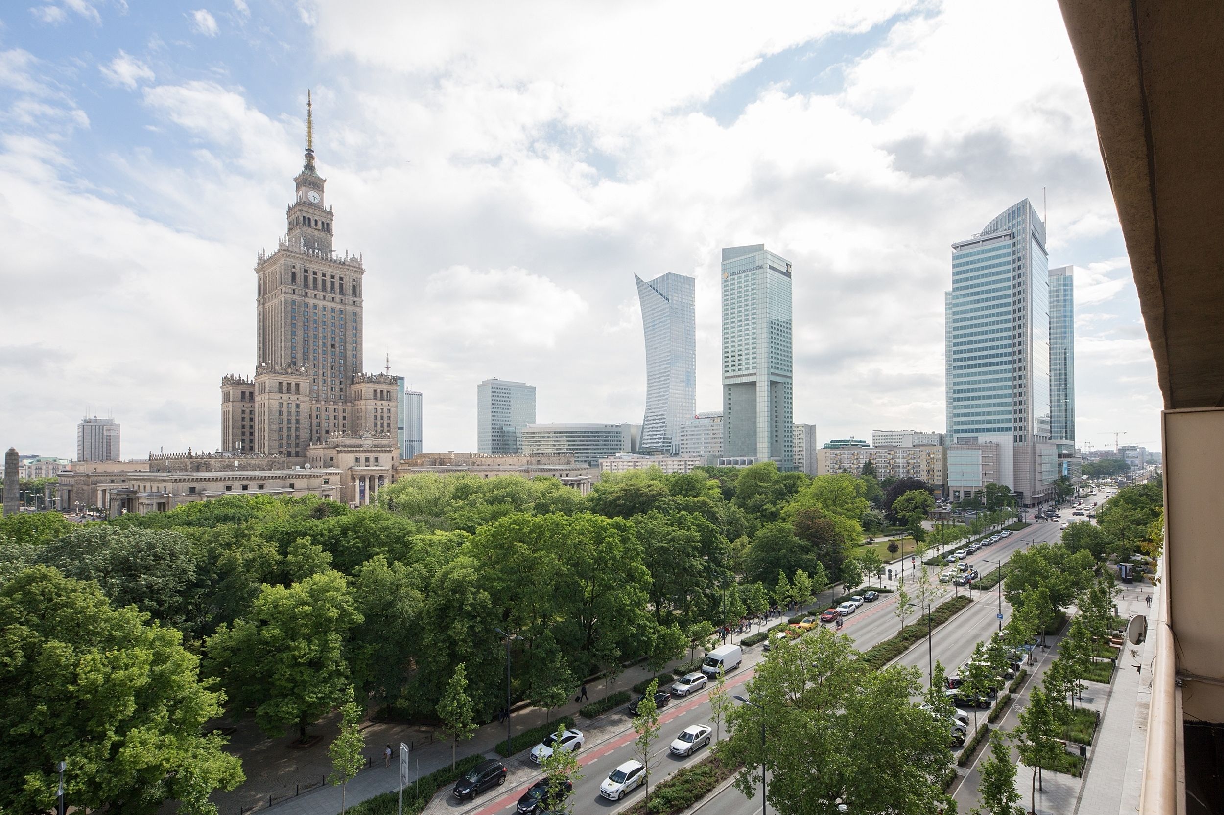 Eine Stadtansicht mit einem historischen Gebäude und modernen Wolkenkratzern, einer von Bäumen gesäumten Straße und blauem Himmel.