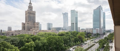 Eine Stadtansicht mit einem historischen Gebäude und modernen Wolkenkratzern, einer von Bäumen gesäumten Straße und blauem Himmel.