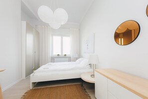 Ein modernes Schlafzimmer mit einem weißen Bett, einem runden Spiegel und einem Holznachttisch.