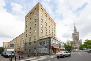 Ein mehrstöckiges Gebäude mit Hauseingang an einer Ecke, einem sichtbaren Schaufenster und einem hohen Turm im Hintergrund.