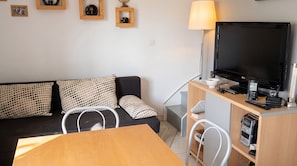 A modern living room with a sofa, a TV, a lamp, and a dining area. - Homerez - House in Le Barcarès, beaches (Le Barcarès)