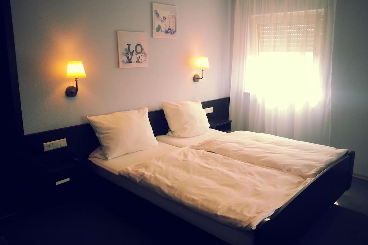 A hotel room with a bed, two wall-mounted lamps, and a window with curtains.