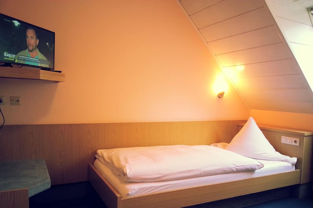 A single bed with a wooden headboard in a room with sloped ceilings.