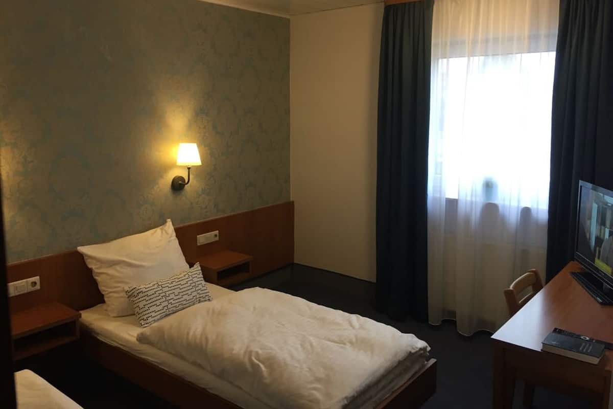 A hotel room with a bed, a desk, a lamp, and a window with curtains.
