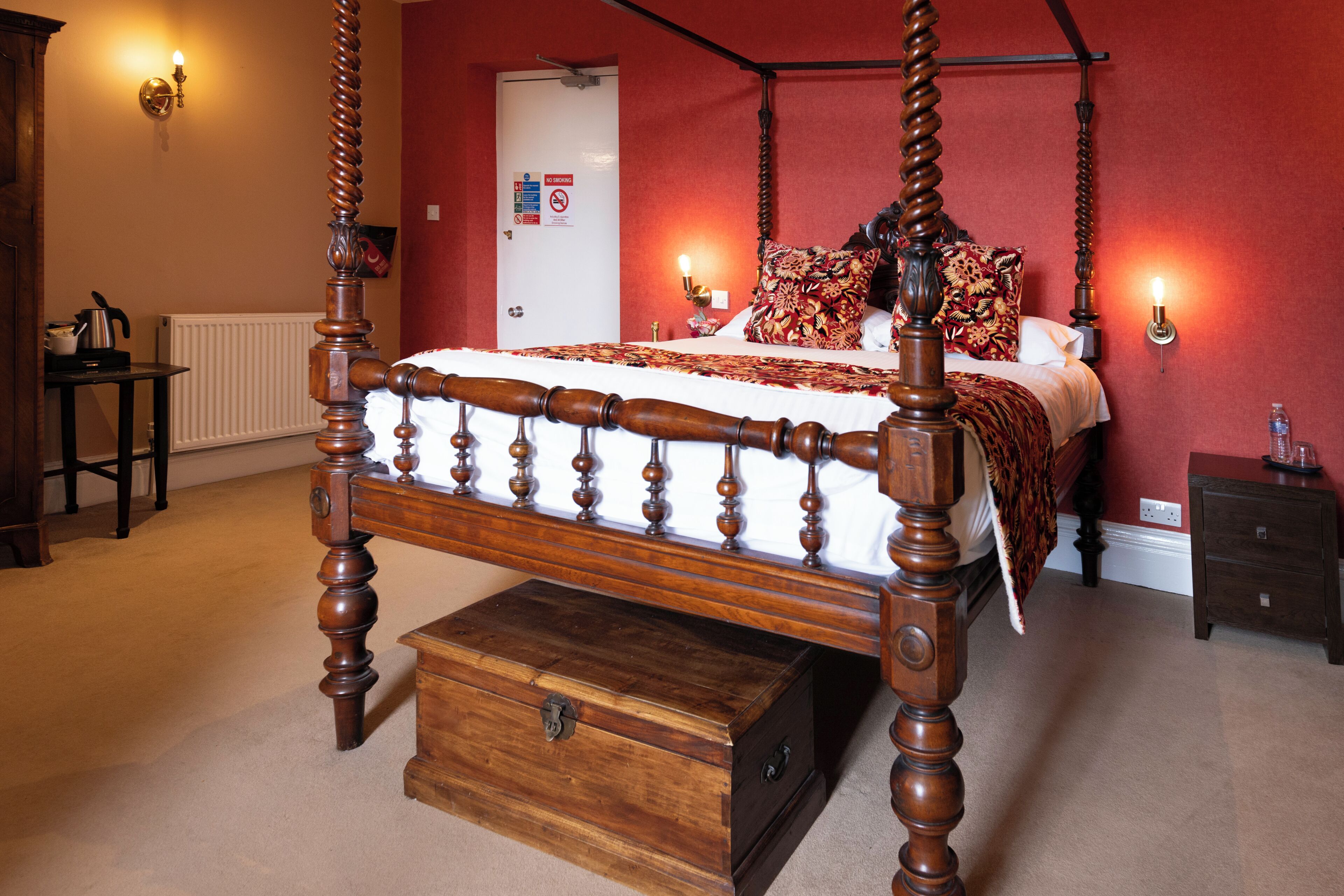 Una cama con dosel y tablero de madera, una mesita de noche y un pequeño cofre de madera.