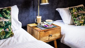 A hotel room with two beds, a nightstand with a lamp, a cup of coffee, and a plate with snacks.