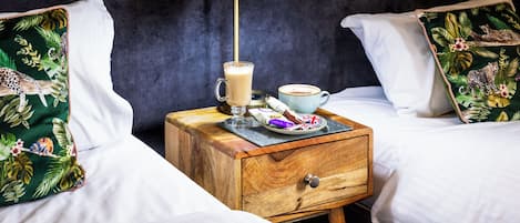 Una habitación de hotel con dos camas, una mesita de noche con lámpara, una taza de café y un plato con aperitivos.