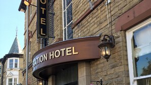 A hotel entrance with a sign reading "Station Hotel," a black awning, and flower baskets on the sidewalk.