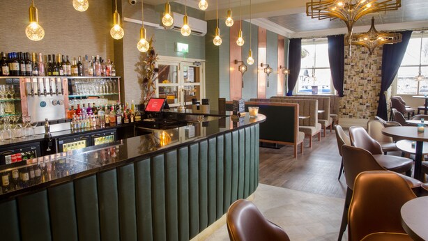 A bar area with a counter, shelves of bottles, and a seating area with chairs and tables.
