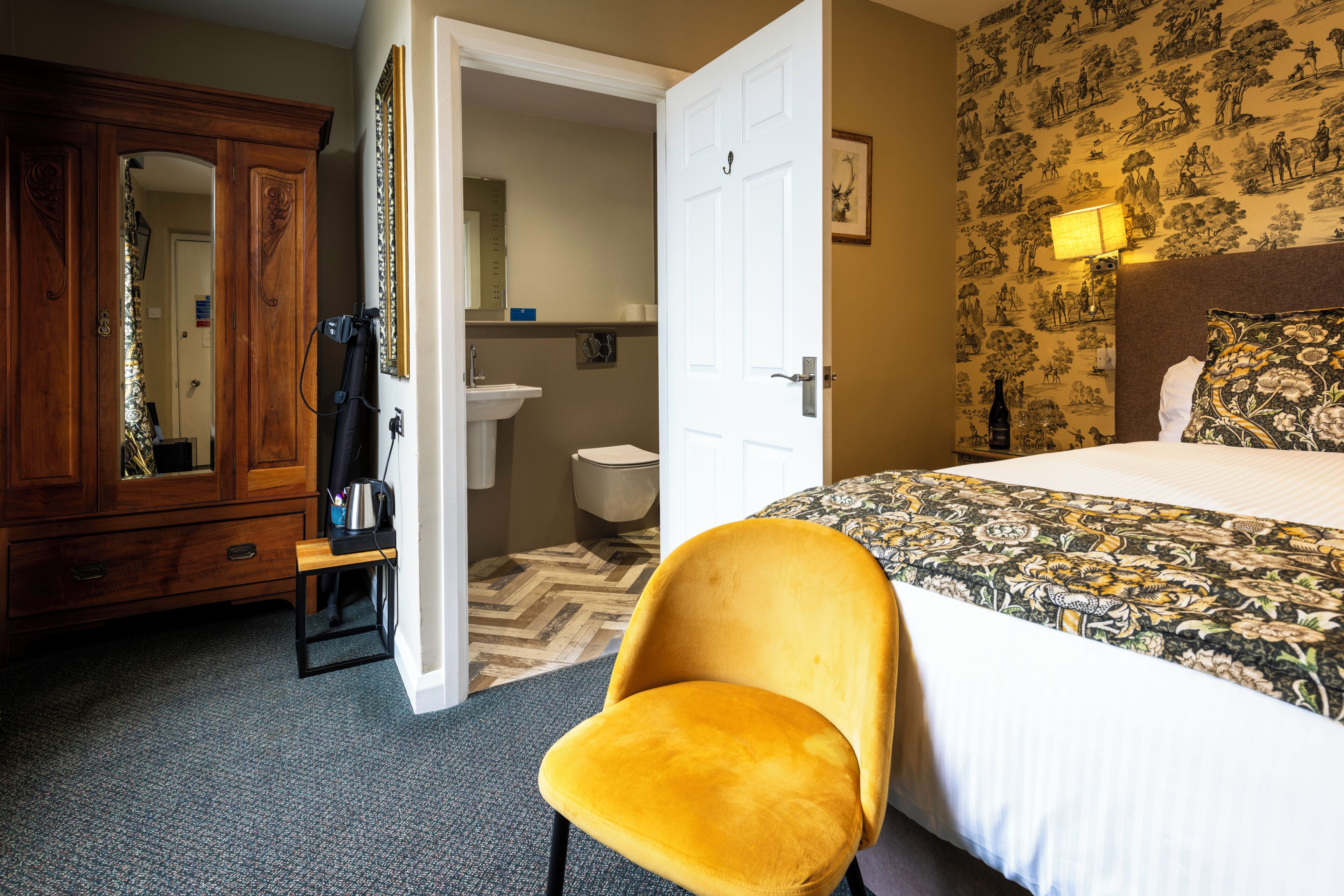 A hotel room with a bed, a wooden wardrobe, a bathroom, and a chair.