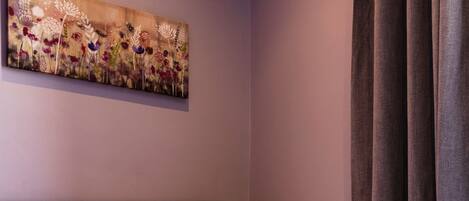 A bedroom with a bed, a purple pillow, a painting on the wall, and a window with curtains.