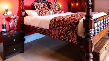 Una cama con dosel con un edredón estampado con motivos florales, una mesita de noche con una botella y vasos, y una pared roja.