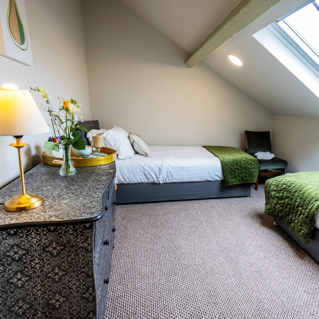 A bedroom with a bed, bedside table, lamp, vase with flowers, and a chair.