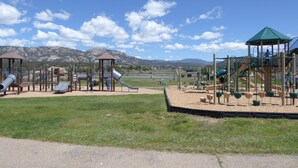 A playground with slides and climbing structures, surrounded by a grassy area and mountains in the background. - Mountain Views, 2 Peaceful Acres, Game Rm, hispeed WiFi, A/C, Comfy Beds 3279 (Estes Park)