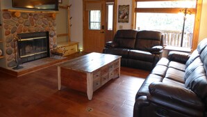 A living room with a stone fireplace, leather sofa, wooden coffee table, and a television mounted on the wall. - Mountain Views, 2 Peaceful Acres, Game Rm, hispeed WiFi, A/C, Comfy Beds 3279 (Estes Park)