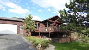 A two-story log cabin with a balcony, a garage, and a stone foundation. - Mountain Views, 2 Peaceful Acres, Game Rm, hispeed WiFi, A/C, Comfy Beds 3279 (Estes Park)