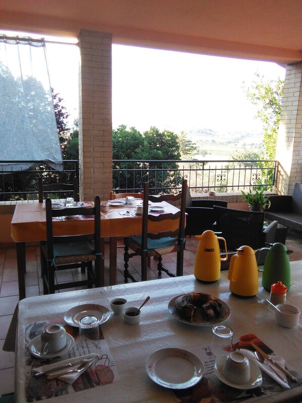 Un espace de restauration en plein air avec une table dressée pour deux personnes, des chaises et une vue sur le paysage.