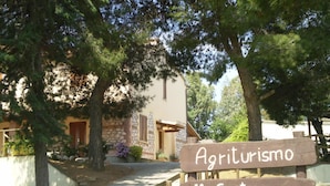 Een houten bord met de tekst 'Agriturismo Il Cantiniere' voor een gebouw met stenen muren en een raam met luiken.