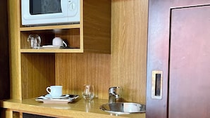 Una kitchenette compacta con microondas, un refrigerador pequeño, un lavamanos y una taza y platillo sobre la encimera.