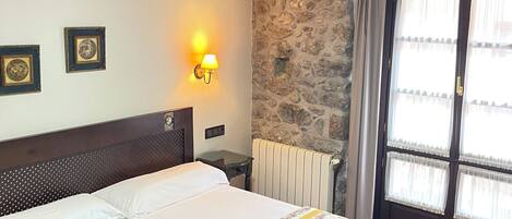 Habitación de hotel con una cama grande, pared de piedra, radiador y ventana con cortinas.