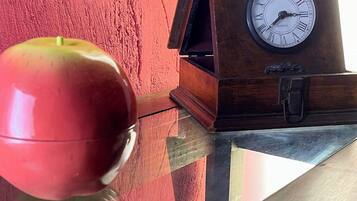 A clock with Roman numerals and a red apple on a reflective surface.