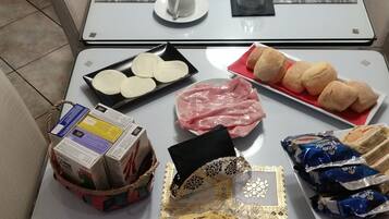 Una mesa de comedor preparada con platos, cubiertos y diferentes alimentos, incluyendo pan, carne y frutas.